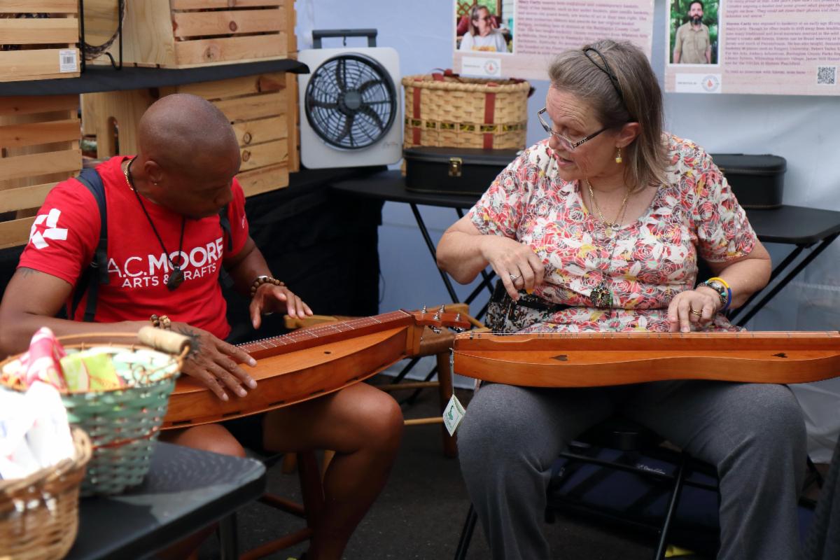Whet up your knife and whistle up your dog! Mary’s got a dulcimer and she’s playing “Groundhog”! A festival attendee intrigued by this Appalachian folk instrument on display in the Carty tent gets a quick tutorial.