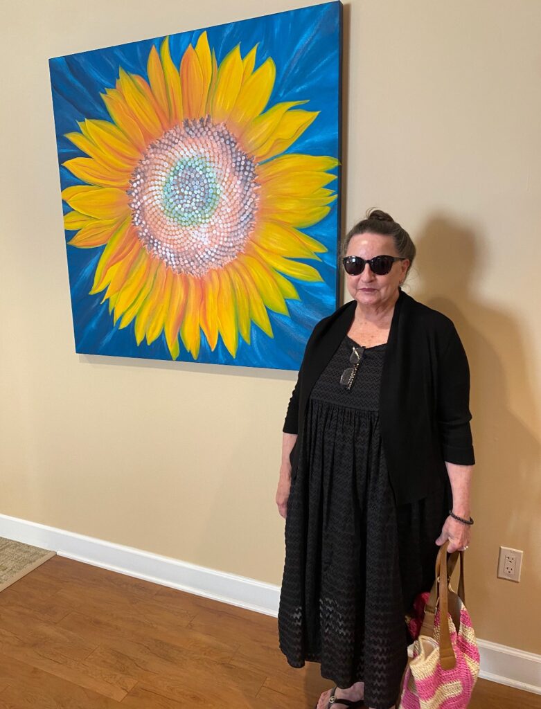 Artist participating in Arts in Healing initiative by Perkins Center for the Arts at Samaritan Hospice center standing in front of their work. 